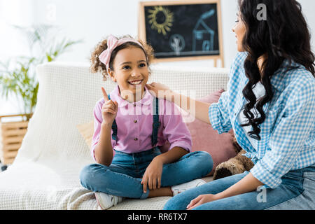 cute african american child showing idea sign while sitting with mother on sofa at home Stock Photo