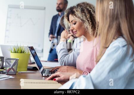 Woman on seminar. Group of young people sitting together at the table while beautiful African woman looking at camera and smiling. Stock Photo