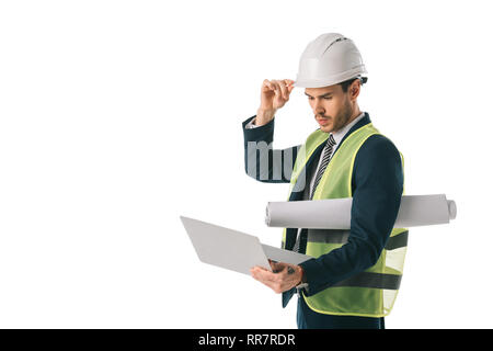 male engineer in hardhat and safety vest holding blueprint and using laptop, isolated on white Stock Photo