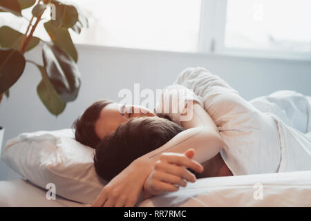 young couple embracing while sleeping in bed with sunlight Stock Photo