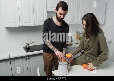 beautiful young couple preparing orange juice during breakfast in kitchen Stock Photo