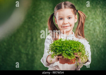 cute smiling child holding flower pot with plant on blurred background, earth day concept Stock Photo