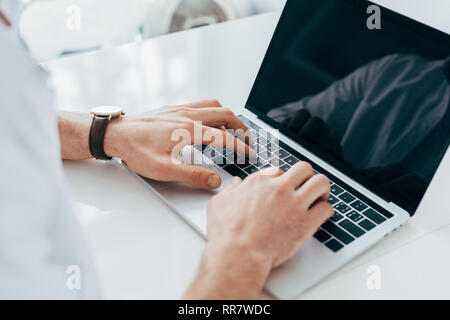 Partial view of man in wristwatch typing on laptop keyboard Stock Photo