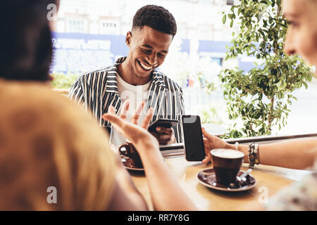Group of creative people meeting up in at cafe. Smiling young friends sitting at coffee shop using smart phones. Stock Photo