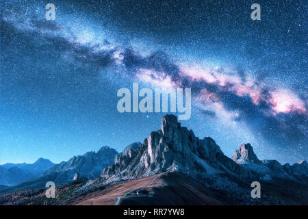 Milky Way above mountains at night in summer. Landscape with alpine mountain valley, blue sky with milky way and stars, buildings on the hill, rocks.  Stock Photo