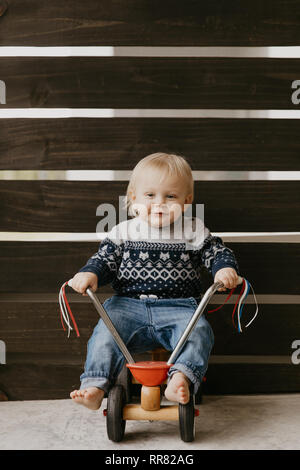 Precious Adorable Cute Little Blonde Baby Toddler Boy Kid Playing Outside on Wooden Toy Bicycle Scooter Mobile Smiling at the Camera and Having Fun Stock Photo