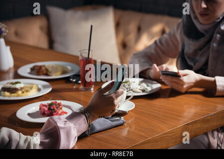 Two Muslim women sit with gadgets at a table in a restaurant Stock Photo