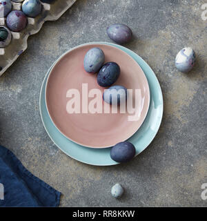 Glazed ceramic plate in a color of Living Coral Pantone with painted violet Easter eggs on a gray stone background, copy space. Top view. Stock Photo