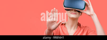 Young woman wearing virtual reality goggles. Woman wearing VR glasses over coral background. VR experience web banner. Stock Photo