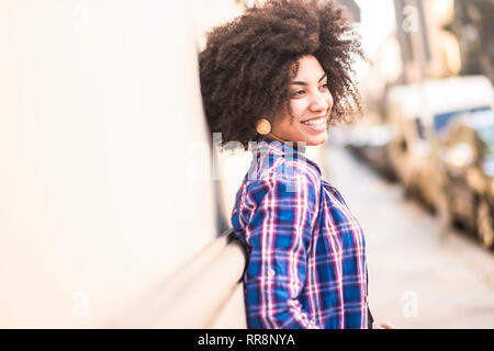 Happy and cheerful young mixed race girl smiling in the city with cars parked in background - bright an dsunny image - attractive woman and happines c Stock Photo