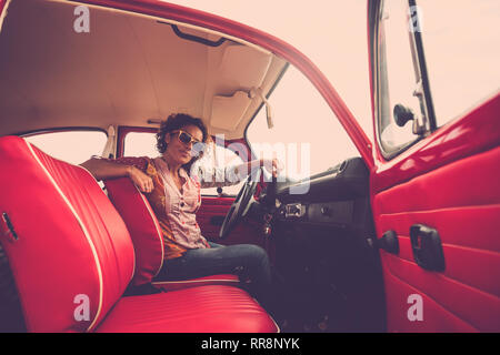 Beautiful middle aged woman looking at you from an old red vintage car Stock Photo