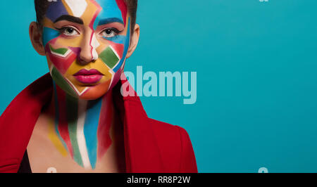 Face of fashion model, looking at camera. Beautiful woman wearing in red jacket. Fashionable girl has creative and colorful pop art make up on face, p Stock Photo