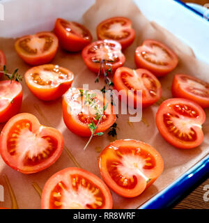 Preparing tomatoes for sun drying or roasting. Cut tomatoes, with fresh thyme and olive oil, on baking parchment in an enamel roasting tin. Square for Stock Photo