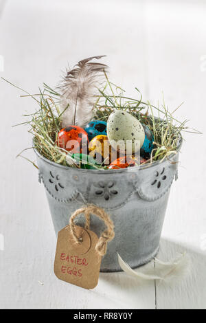 Various Easter eggs with feathers and hay on white table Stock Photo