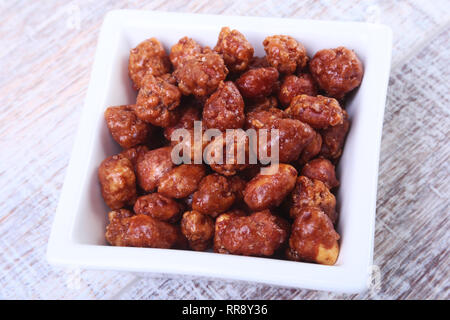 Sugared Hazelnuts in a white bowl on a wooden background. Hazelnuts in sugar glaze. Selective focus. Stock Photo