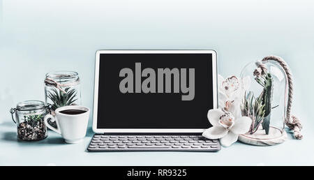 Blank screen modern laptop computer with succulent plants in glasses and orchid flowers on table.  Home female business office workspace.  Black blank Stock Photo