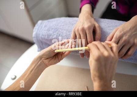 Over the shoulder view of professional manicurist filing nails of a woman in a manicure treatment. Stock Photo