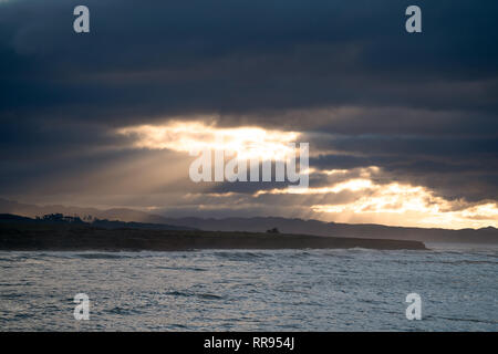 Early morning sunrise with light rays streaming out of an opening in the clouds, illuminating the coastline near Cambria, San Simeon, California. Stock Photo