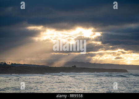 Early morning sunrise with light rays streaming out of an opening in the clouds, illuminating the coastline near Cambria, San Simeon, California. Stock Photo