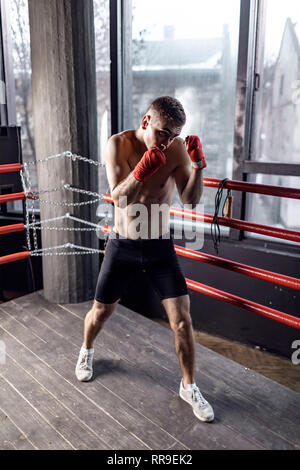 Athletic boxer man with red bandages on hands in the ring Stock Photo