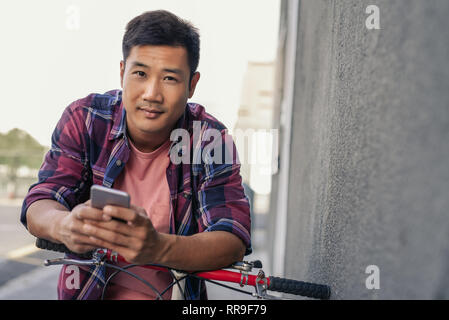Smiling young man leaning over his bike reading a text Stock Photo