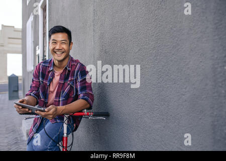 Smiling young man leaning on his bicycle using a tablet Stock Photo