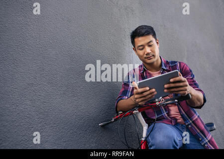 Young man leaning on his bicycle using a tablet Stock Photo