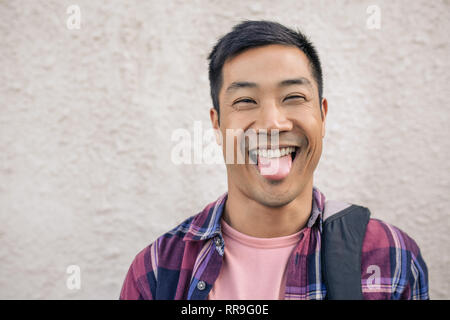 Smiling young Asian man standing outside sticking out his tongue Stock Photo