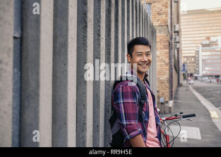 Smiling young man leaning against a wall with his bicycle Stock Photo