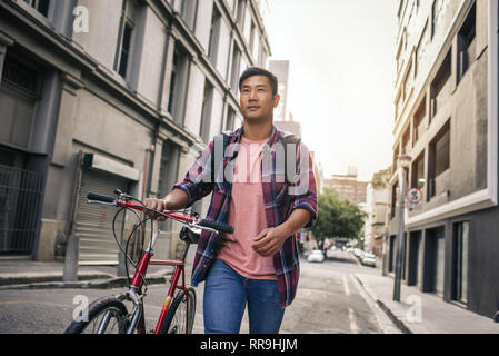 Young man walking with his bike down a city street Stock Photo