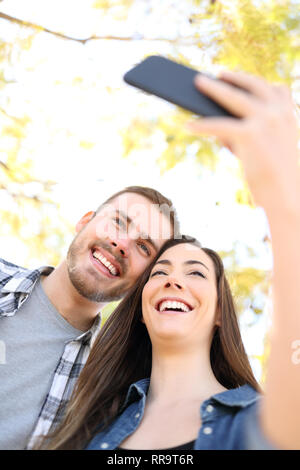 Happy couple taking selfies with smartphone in a park with trees in the background Stock Photo