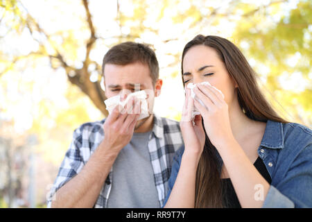 Sick couple sneezing together covering mouth with wipes in a park Stock Photo
