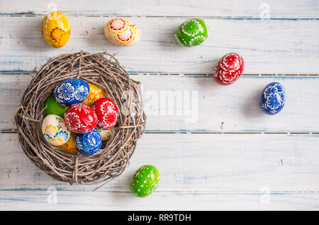 Close-up multicolored easter eggs in basket on wooden table. Stock Photo