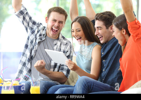 Excited group of friends watching media on tablet sitting on a couch in the living room at home Stock Photo