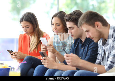Group of serious friends using their smart phones sitting on a couch in the living room at home Stock Photo