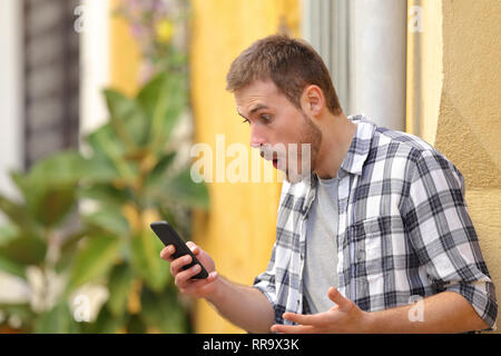 Surprised man using smart phone finding amazing content standing in a colorful street Stock Photo