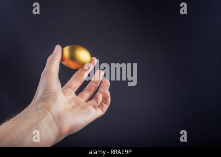 Man hand holding Golden egg on a black background Stock Photo