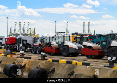 Asphalt roller and trucks waiting loading on a ship for import or export Stock Photo