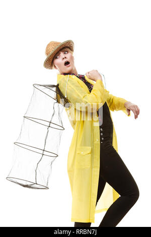 Spinning, angling, cheerful fisherwoman concept. Happy woman in yellow raincoat holding empty fishing keepnet, having fun. Stock Photo