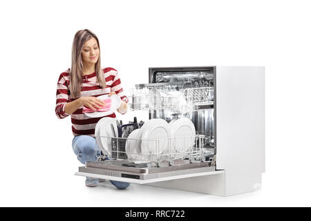 Young woman wiping a plate next to a dishwasher isolated on white background Stock Photo