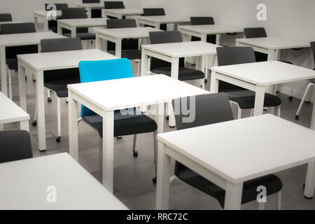 Classroom with black chairs and one blue chair. Hiring, vacant or choosing concept. White desks or tables Stock Photo