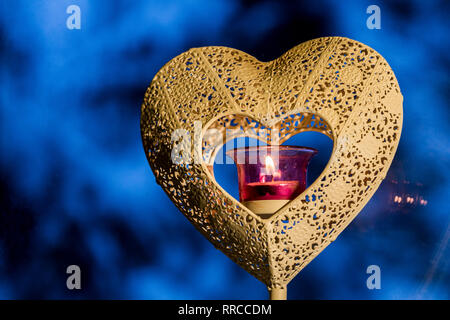 Heart in heart candle holder with candle flame in the core on blue winter background. Stock Photo