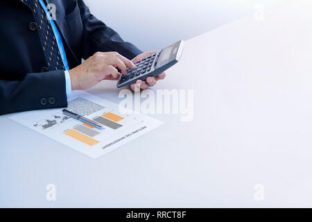 Businessmen isolated on white using calculator reviewing financial report for a return on investment or investment risk analysis on a white desk. Stock Photo