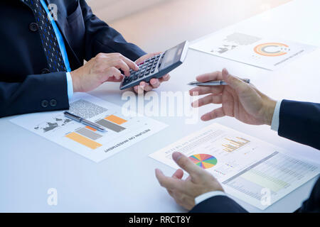 Two businessmen are deeply reviewing a financial reports for a return on investment or investment risk analysis on a white desk. Upper and lower right Stock Photo