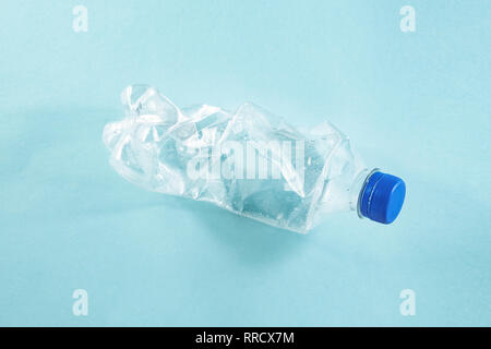 Plastic waste concept: discarded crumpled water bottle in blue background, detailed view. A thrown away single use plastic bottle depicting excessive  Stock Photo