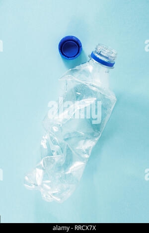 Plastic waste concept: discarded crumpled water bottle in blue background, detailed view.Top view of a thrown away single use plastic bottle depicting Stock Photo