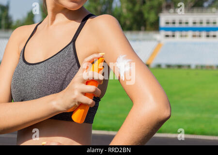 Young female runner standing and putting sun lotion on hand. Girl using sunscream before sport running exercise on summer morning. Sports and healthy  Stock Photo