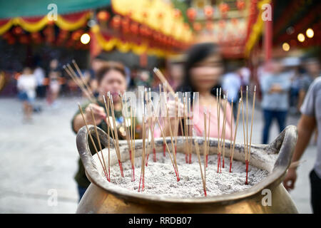 Asian people are putting burning incense sticks in the large golden pot on the blurred background of the decorated street during the celebration of Lu Stock Photo