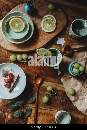 From above of beautiful ceramic plates and cups with slices of lemon and grapes in composition on wooden table Stock Photo