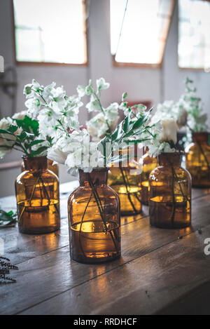 Set of light bloom branches in retro glass vases with water on wooden table in room Stock Photo